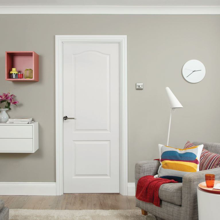 Modern interior design with a white Camden door in the center, a gray sofa, colorful pillows, and a green wall.