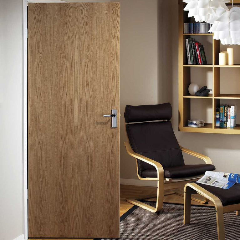 An oak door in a room with a black chair and a bookshelf.