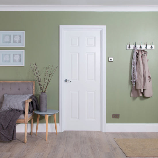 Living room with green walls, a white 6-panel smooth door, and a gray sofa.