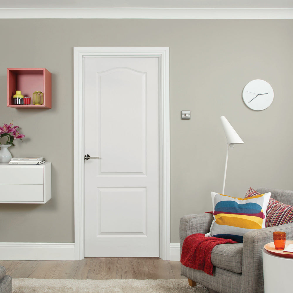 Modern interior design with a white Camden door in the center, a gray sofa, colorful pillows, and a green wall.