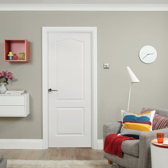 Modern interior design with a white Camden door in the center, a gray sofa, colorful pillows, and a green wall.