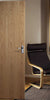 An oak door in a room with a black chair and a bookshelf.
