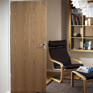 An oak door in a room with a black chair and a bookshelf.